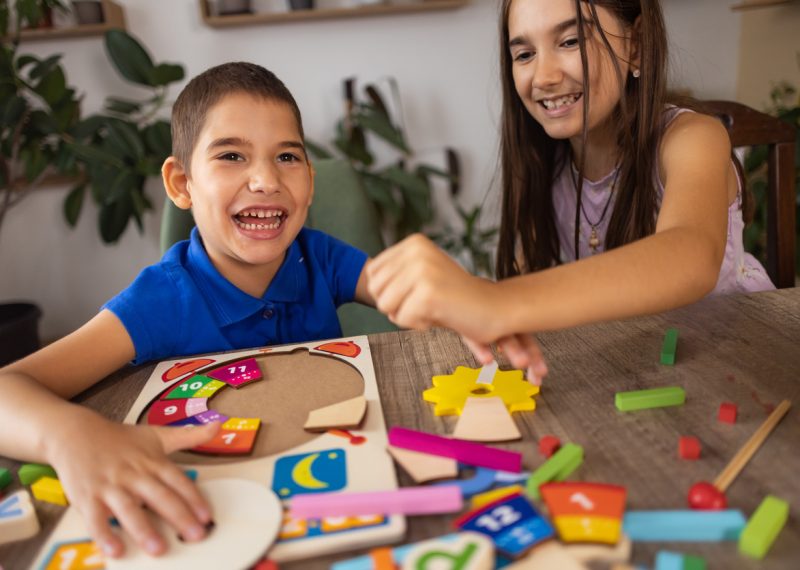 Autism & Inclusion - creating a more welcoming world. A small dark-haired boy with autism plays with his older sister.