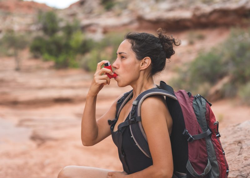 A young ethnic female takes a short break from her day hike in the Utah desert to use her inhaler.